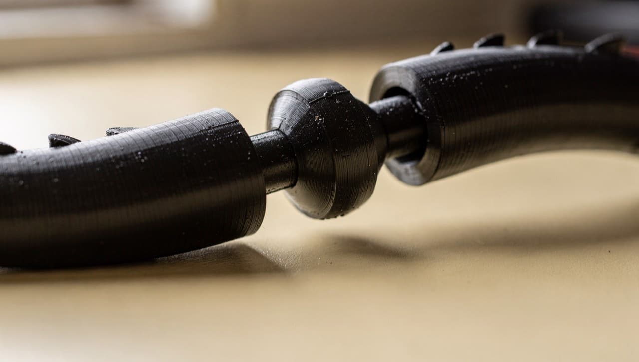Macro close-up of three connected segments on a 3D-printed articulated dragon, showing the print-in-place ball-and-socket joint mechanism between each matte black segment.